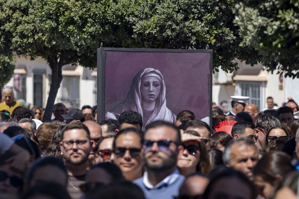 Cientos de personas esperan la salida de los pasos de la Hermandad de El Perdón mientras rodean un cartel con la imagen de una virgen durante la Semana Santa de 2026 en San Fernando Cádiz, España.