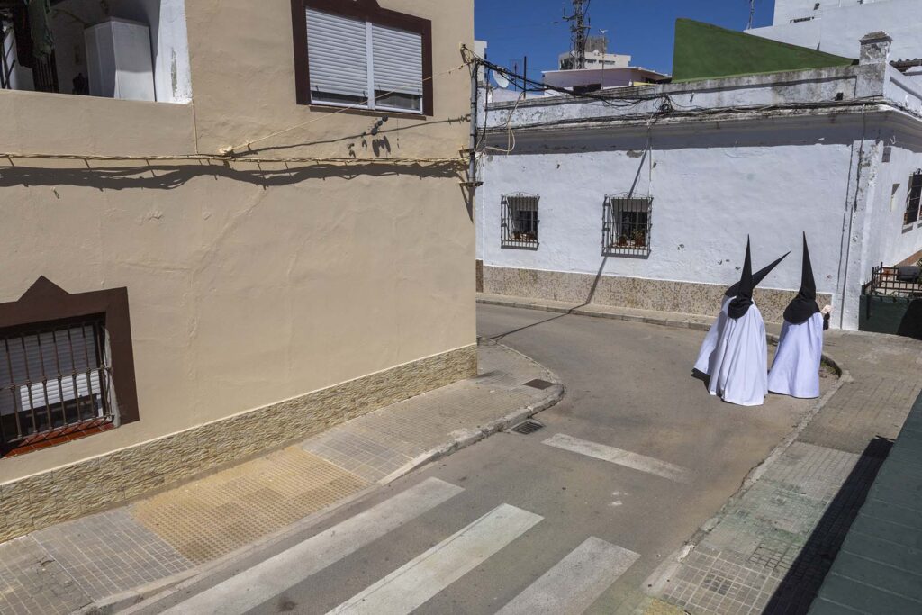 Tres penitentes ataviados con sus túnicas y capirotes se dirigen a la iglesia desde donde salen los pasos de El Perdón en San Fernando, Cádiz, España durante la Semana Santa 2026 en la Bahía de Cádiz.