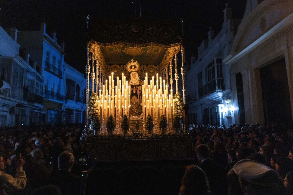 El paso de la virgen de la Hermandad de La Expiración atraviésales las calles de San Fernando en Cádiz, España bajo una impresionante oscuridad únicamente iluminada por las velas de su propio paso mientras cientos de personas se agolpan a su alrededor para contemplarla durante la Semana Santa 2026 en la Bahía de Cádiz.