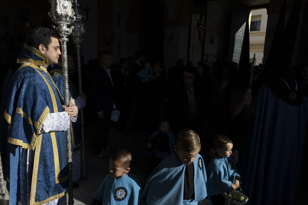Niños y adultos penitentes esperando la salida de la procesión de la Hermandad de La Misericordia en una foto con enorme fuerza visual por el contraste de los colores saturados en San Fernando, Cádiz, España durante la Semana Santa 2026 en la Bahía de Cádiz.