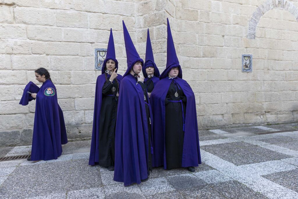 Un grupo de mujeres penitentes vestidas con sus llamativas túnicas moradas esperan en el patio de La Prioral la salida de la procesión de la Hermandad de la Soledad en El Puerto de Santa María, Cádiz, España durante la celebración de la Semana Santa 2026 en la Bahía de Cádiz.